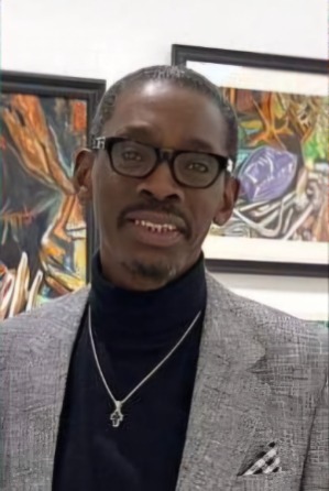 Photo of a man standing in front of artwork wearing a grey blazer and glasses